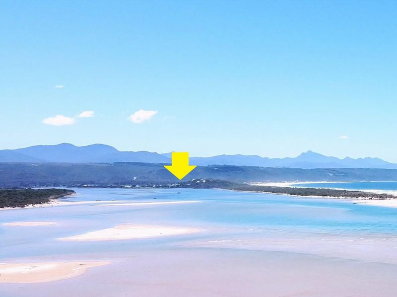 A wide aerial view of the coastal landscape and estuary, highlighting the property location with a yellow arrow.