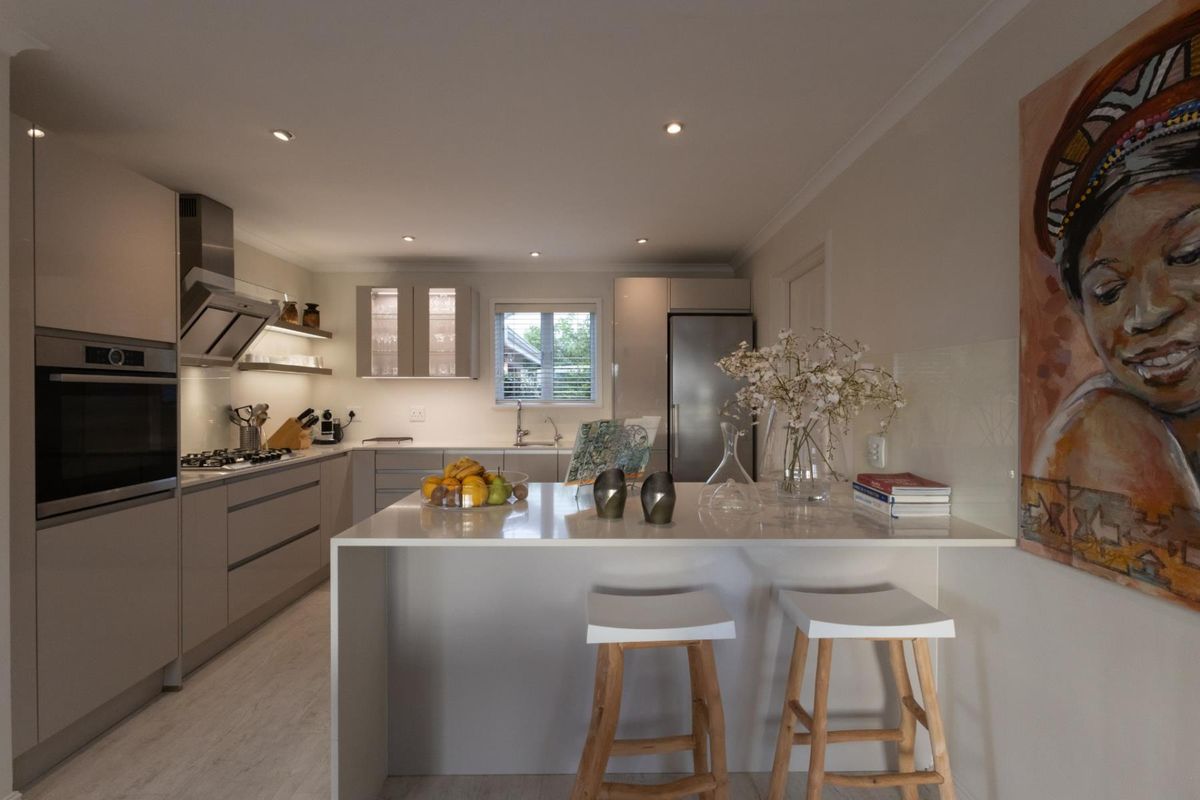 Modern kitchen featuring sleek cabinetry, integrated oven, gas hob, extractor fan, and a central island with a stone countertop.
