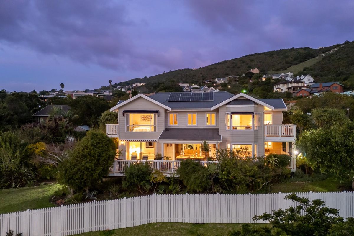 A beautiful two-story residential home featuring a wrap-around balcony, solar panels, and a well-maintained garden, captured during the twilight hour.