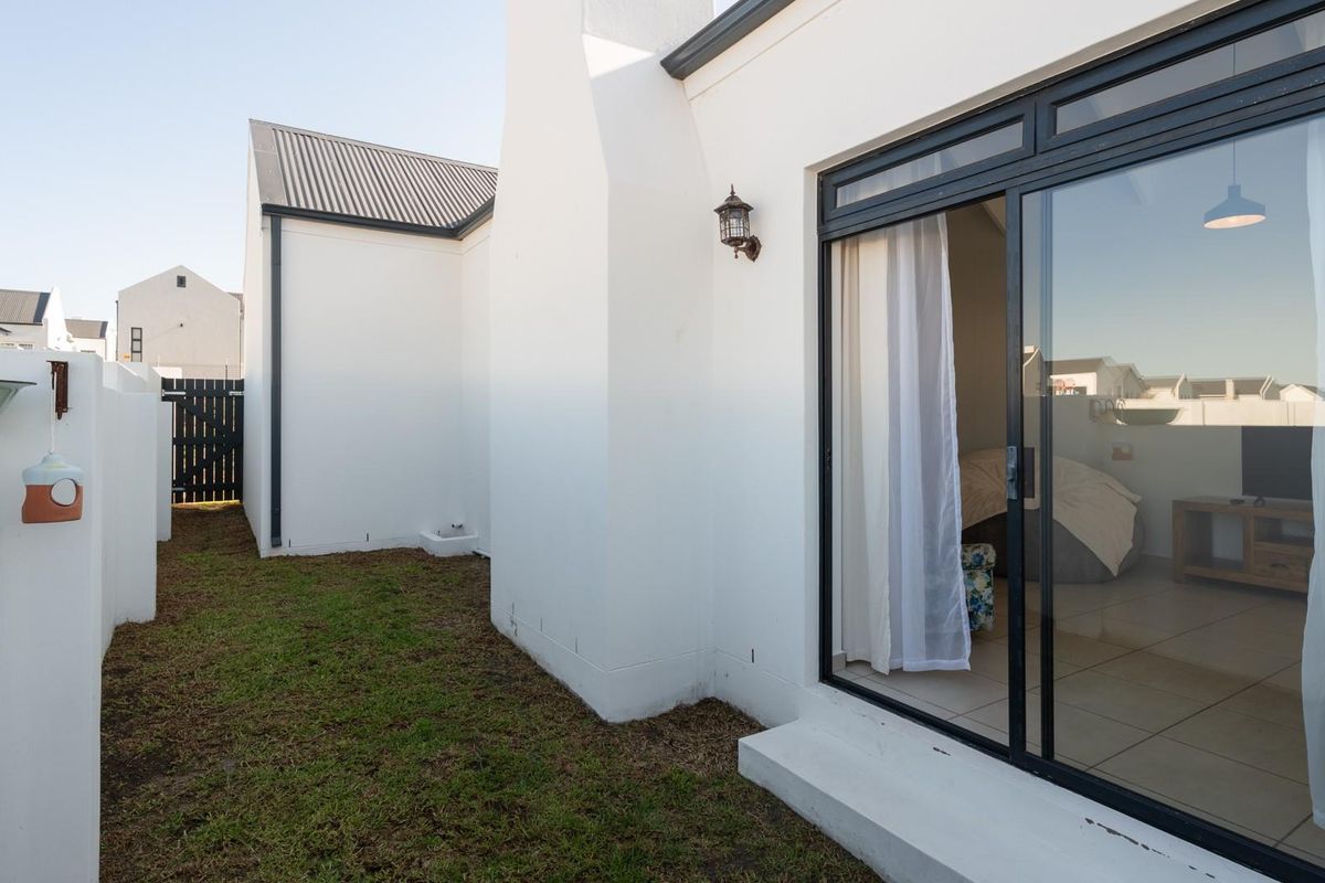 A view of the rear exterior area featuring a small lawn, white plastered walls, and a large sliding glass door leading into the interior.