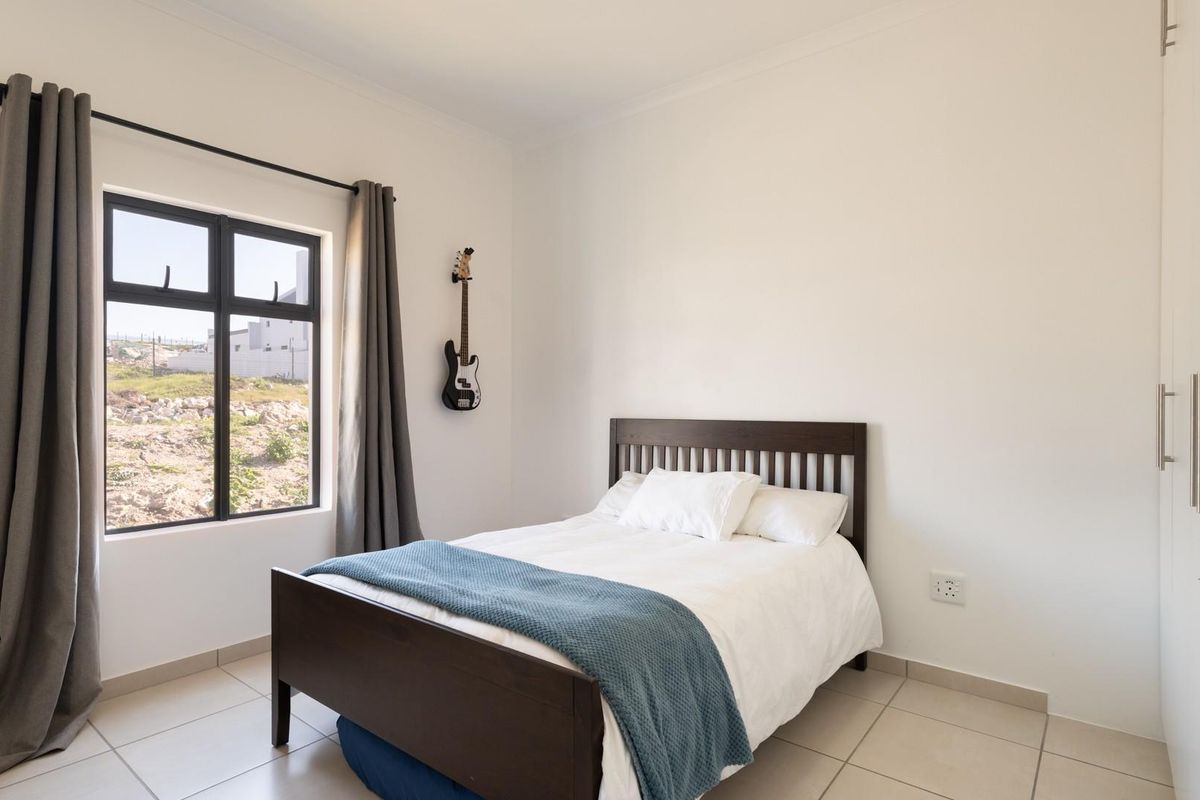 A bright and well-maintained bedroom featuring neutral tiled flooring, built-in cupboards, and a large window providing natural light.