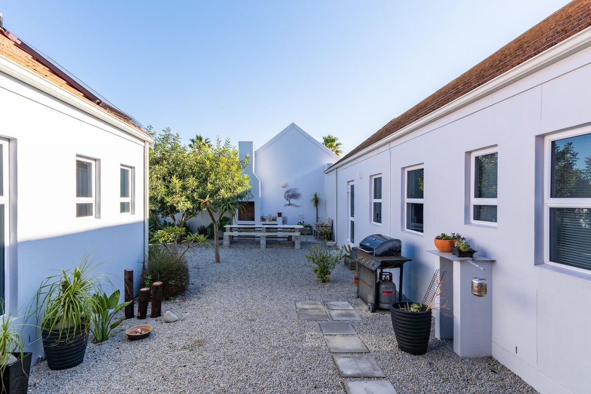 A well-maintained rear courtyard featuring a gravel surface, paved stepping stones, and a built-in outdoor fireplace nestled between two wings of the house.