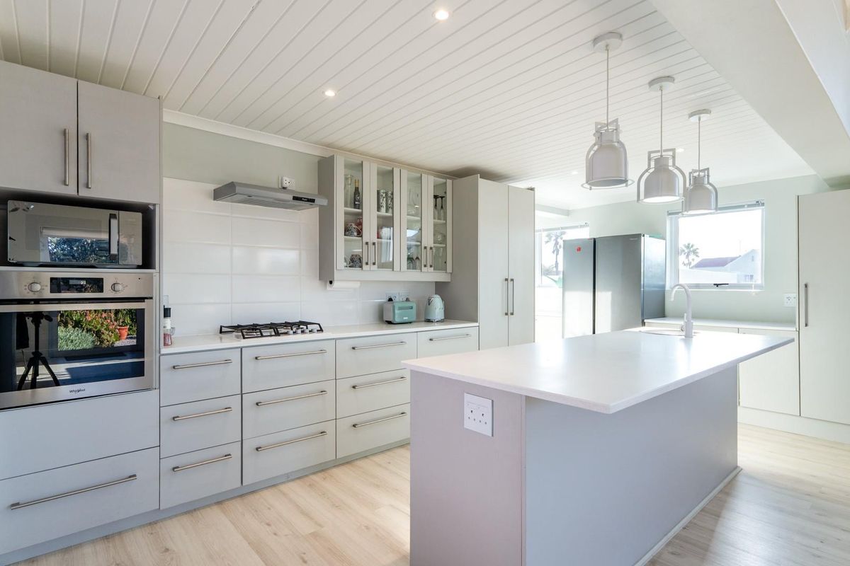 Modern kitchen featuring light grey shaker cabinetry, quartz countertops, a central island, built-in appliances, and a bright tongue and groove ceiling.