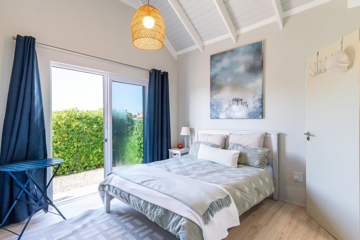 Bright bedroom featuring vaulted ceilings with exposed rafters, laminate flooring, and a sliding glass door providing direct access to the garden.