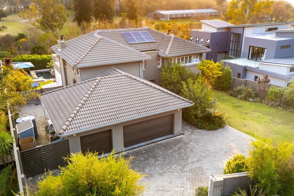 Aerial view of a modern residential property featuring a tiled roof with solar panels, a double garage, and a landscaped garden.