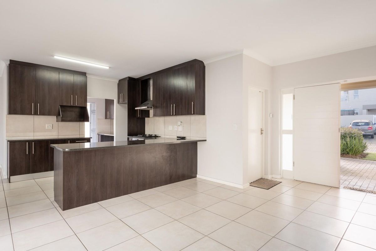 Modern open-plan kitchen featuring dark wood cabinetry, granite countertops, built-in hob, extractor fan, and tiled flooring, with direct access to the exterior.