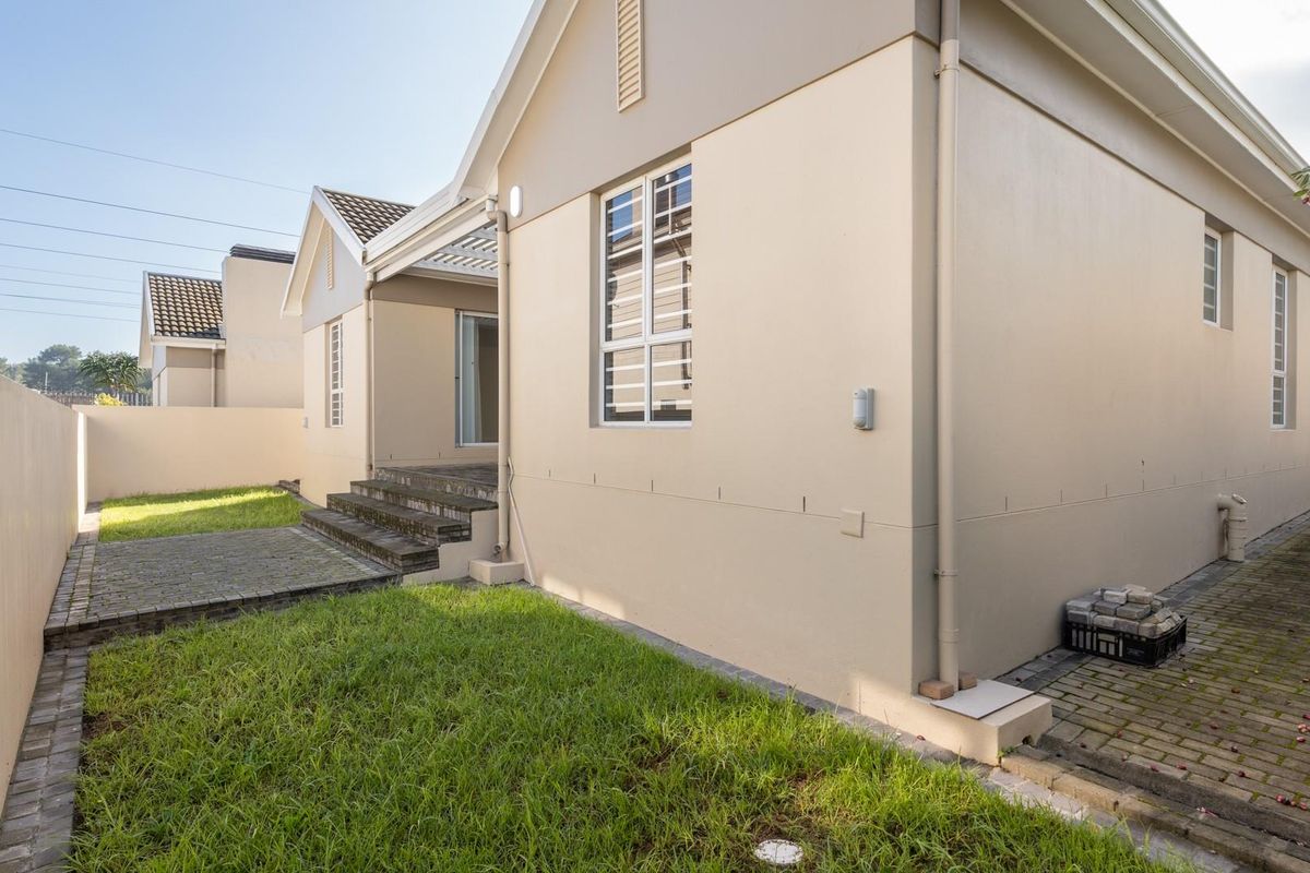 Rear view of the property featuring a paved walkway, small lawn area, boundary wall, and access to the interior via a sliding door.
