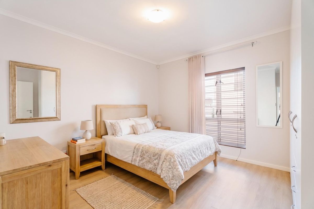 A well-maintained bedroom featuring light laminate flooring, built-in wardrobe storage, and venetian blinds for adjustable natural light.