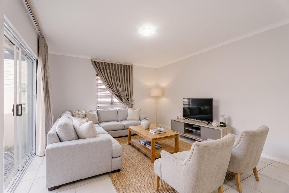A bright and well-maintained living room featuring neutral tiled flooring, large sliding glass doors providing natural light, and clean, modern finishes.