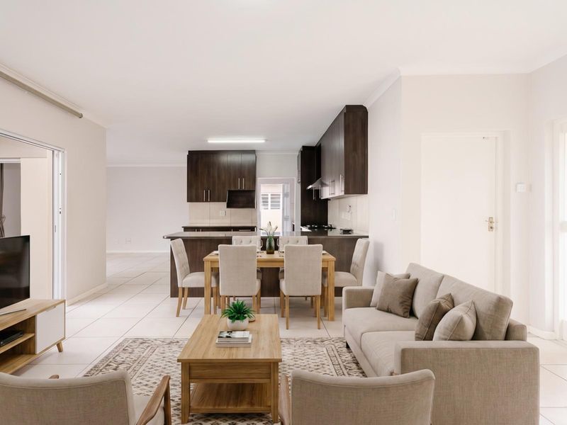 Spacious open-plan living and dining area featuring a modern kitchen with dark wood cabinetry, built-in appliances, and neutral tiled flooring throughout.