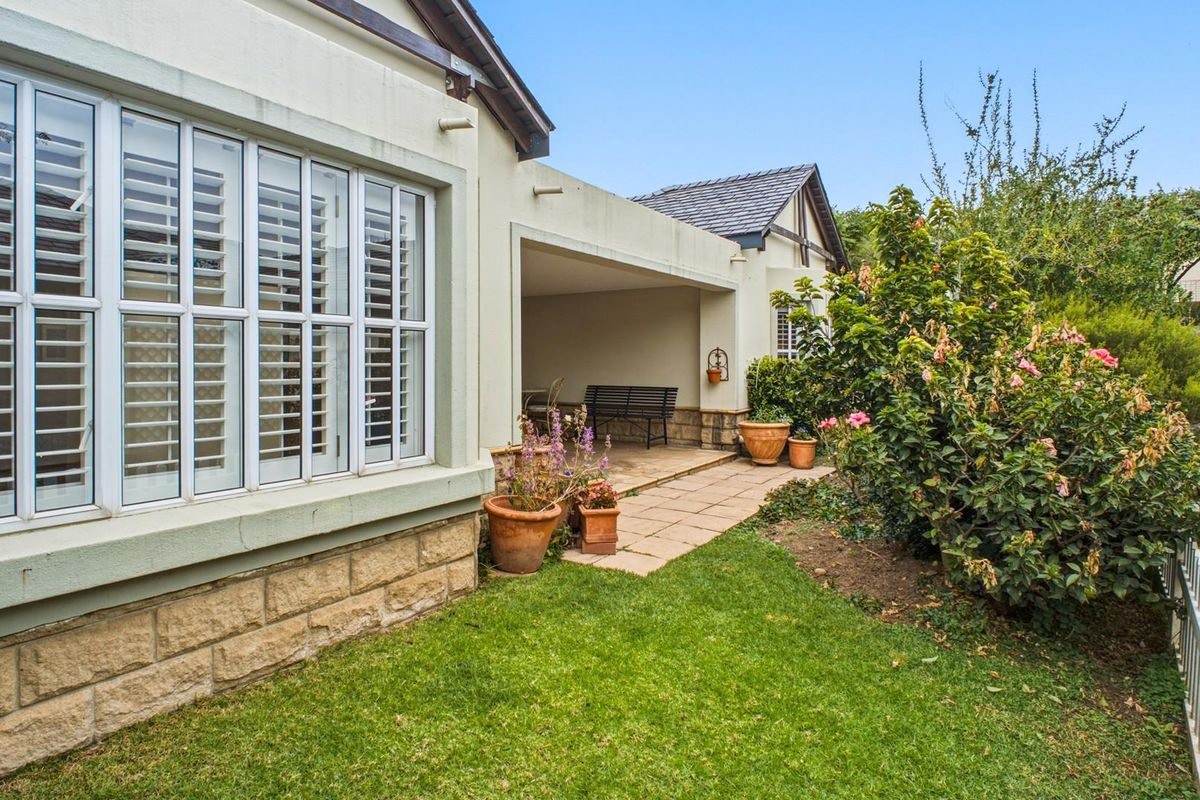 A well-maintained rear exterior view featuring a covered patio area, stone-clad foundation detailing, and established garden landscaping.