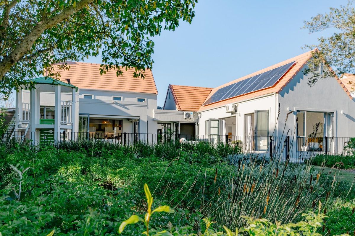 Rear view of a well-maintained house featuring terracotta roof tiles, solar panels, bi-fold doors, and a lush landscaped garden.