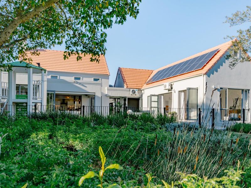 Rear view of a well-maintained house featuring terracotta roof tiles, solar panels, bi-fold doors, and a lush landscaped garden.