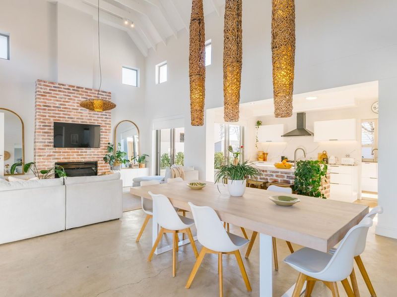 Spacious open-plan living and dining area featuring a vaulted ceiling, polished concrete floors, and a striking exposed brick fireplace, seamlessly connected to a modern kitchen.