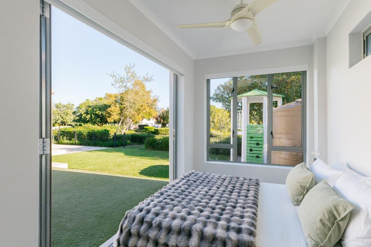 Bright bedroom featuring a ceiling fan and large sliding glass doors that open directly onto a private garden area.