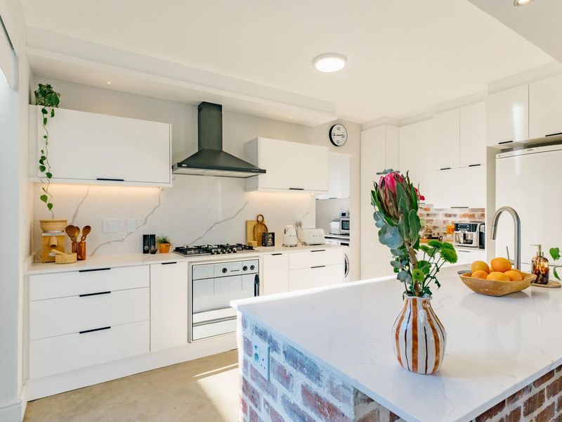 Modern kitchen featuring white cabinetry, stone countertops, a central island with an exposed brick base, gas hob, and integrated extractor fan.
