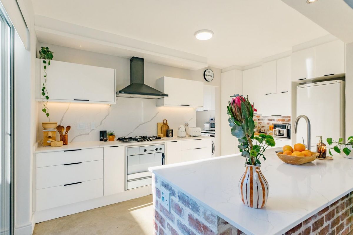 Modern kitchen featuring white cabinetry, stone countertops, a central island with an exposed brick base, gas hob, and integrated extractor fan.