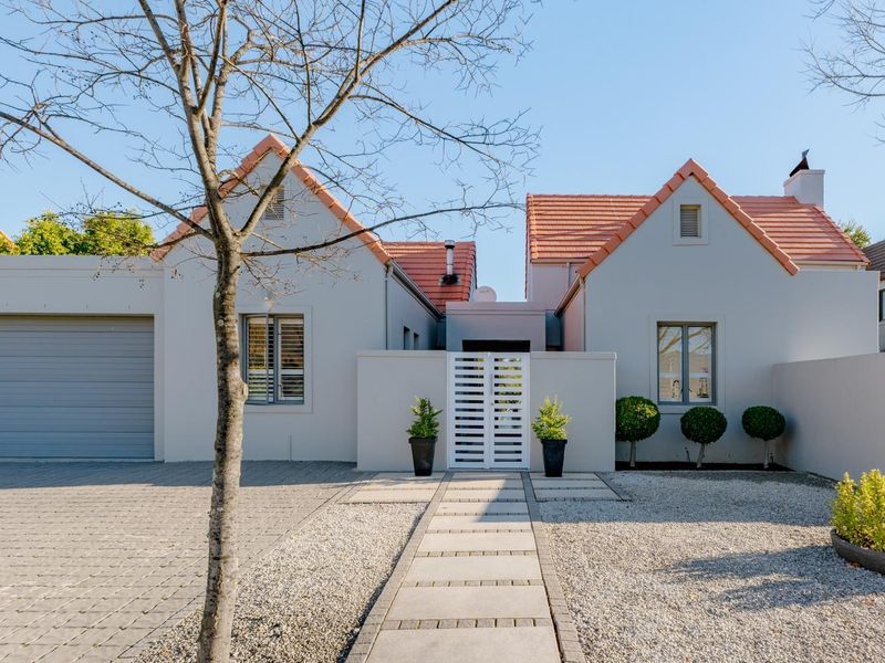 Front elevation of a well-maintained house featuring a paved driveway, double garage, and a neat pedestrian entrance with a concrete walkway.