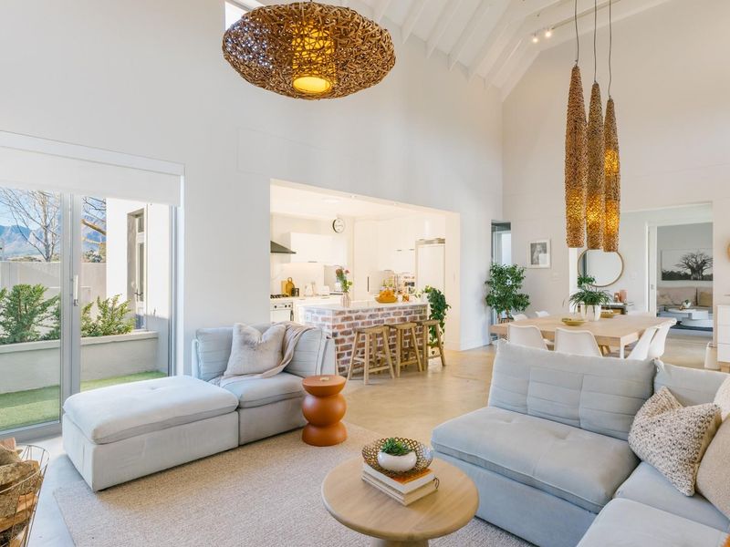 Spacious open-plan living area featuring a vaulted ceiling, exposed brick kitchen island, and seamless flow to the outdoor patio through large sliding glass doors.