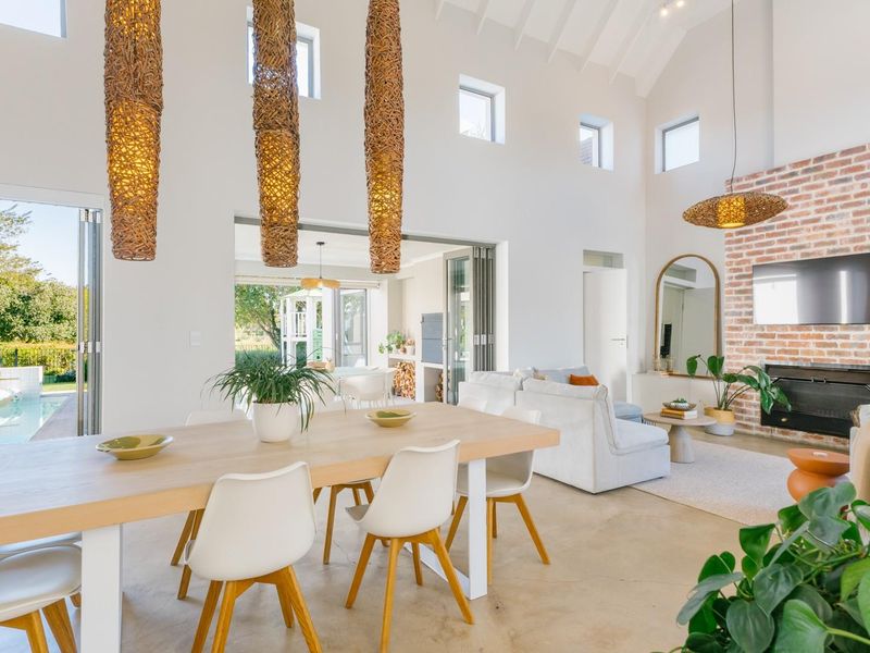 Spacious open-plan living and dining area featuring a vaulted ceiling, exposed brick fireplace, polished concrete floors, and seamless access to the outdoor pool area.
