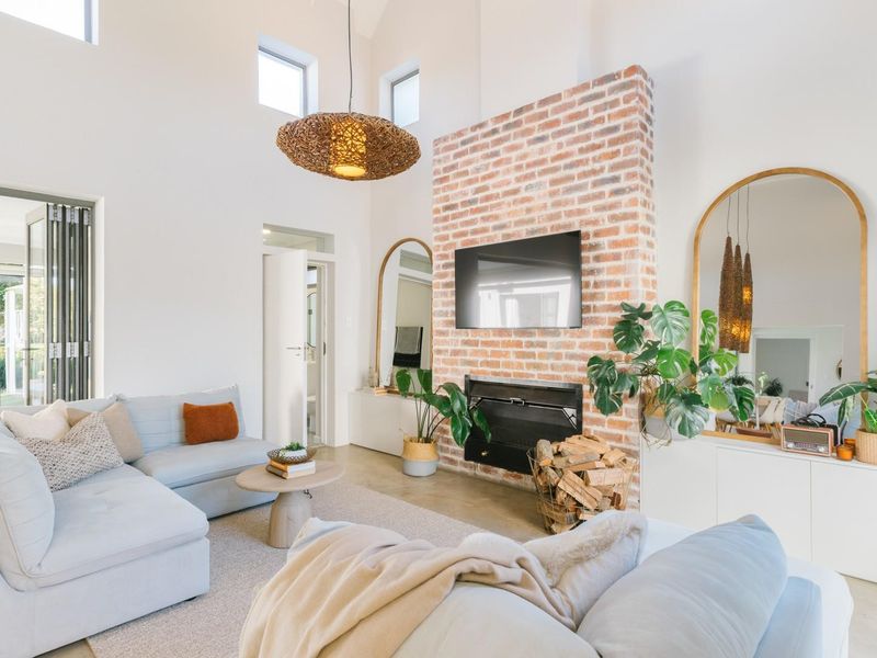 Spacious living room featuring a striking exposed brick fireplace, vaulted ceilings, and bi-fold doors that open to an outdoor area.