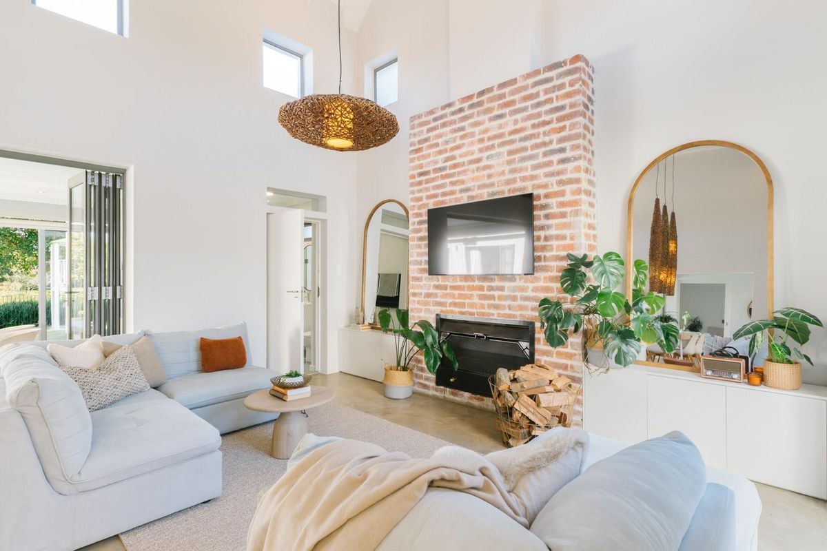 Spacious living room featuring a striking exposed brick fireplace, vaulted ceilings, and bi-fold doors that open to an outdoor area.