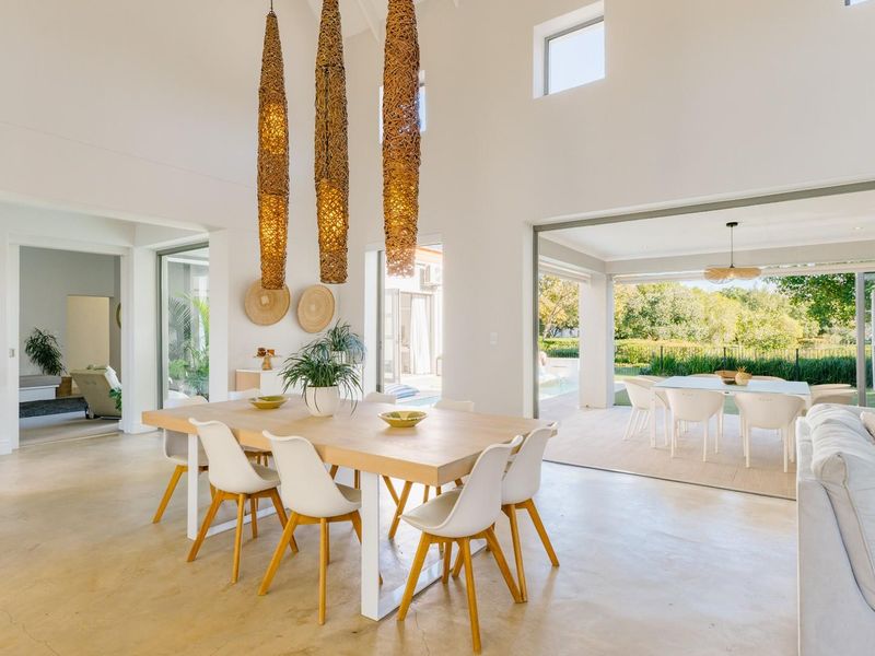 Spacious open-plan living and dining area featuring polished concrete floors, vaulted ceilings, and seamless indoor-outdoor flow through large stacking glass doors.