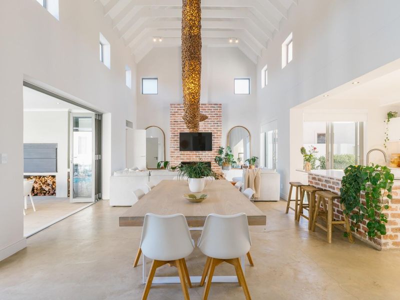 Spacious open-plan living, dining, and kitchen area featuring a vaulted ceiling, exposed brick fireplace, and seamless flow to the outdoor patio through bi-fold doors.