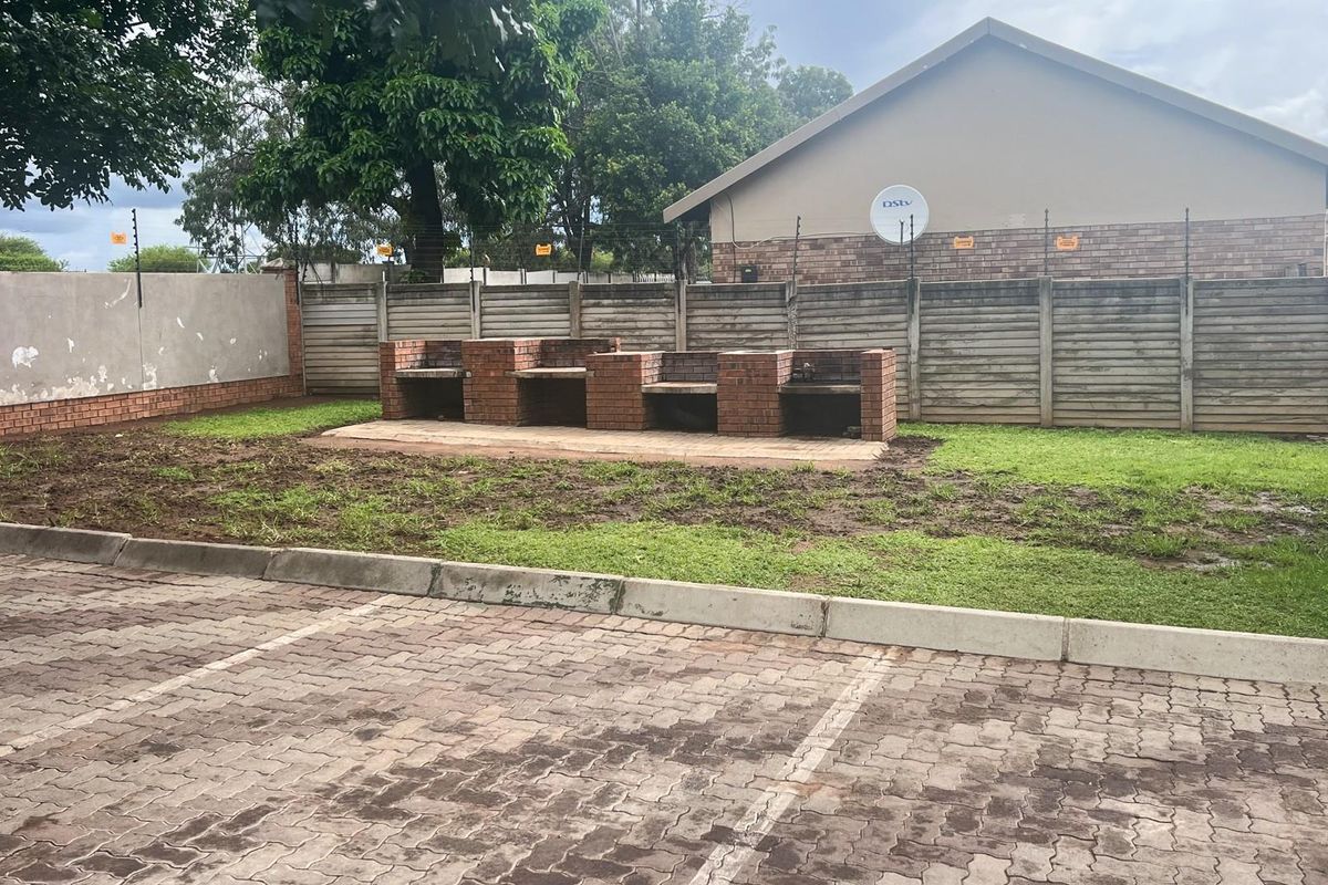 Communal outdoor area featuring a built-in brick braai facility, paved parking area, and perimeter walling with electric fencing.