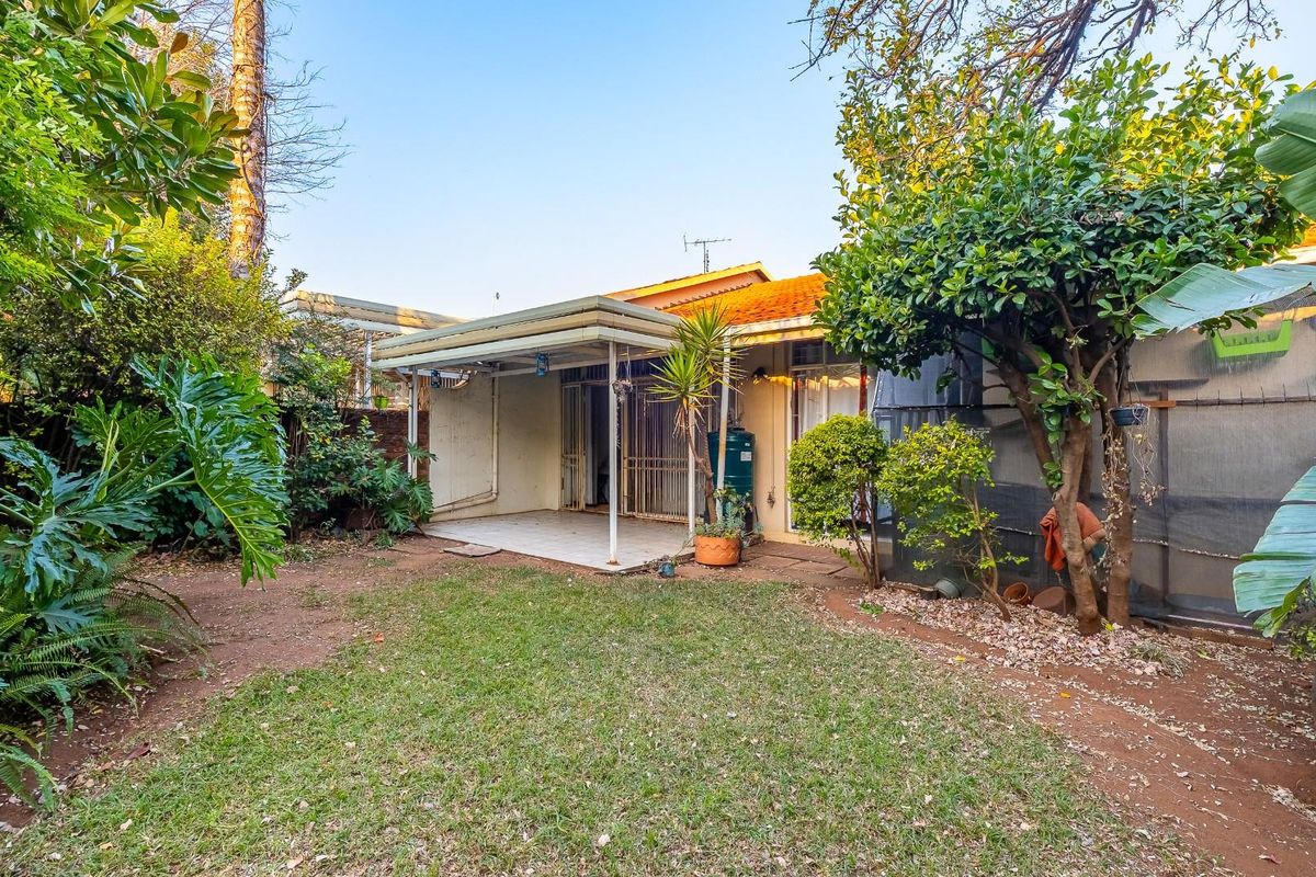 Rear view of the townhouse featuring a covered patio area, tiled flooring, and a private garden space with established trees and shrubs.