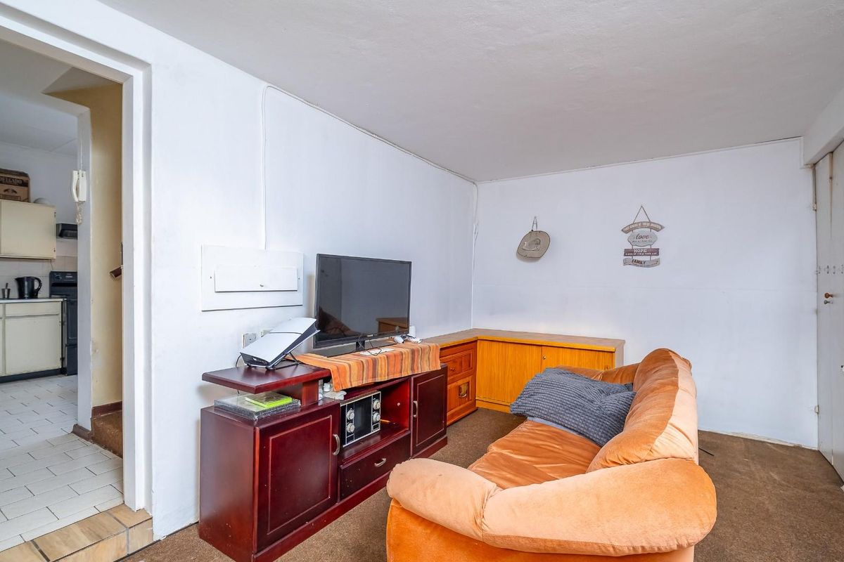 A living room area with carpeted flooring, featuring an adjacent kitchen view. The space requires cosmetic updates to modernize the interior finishes.