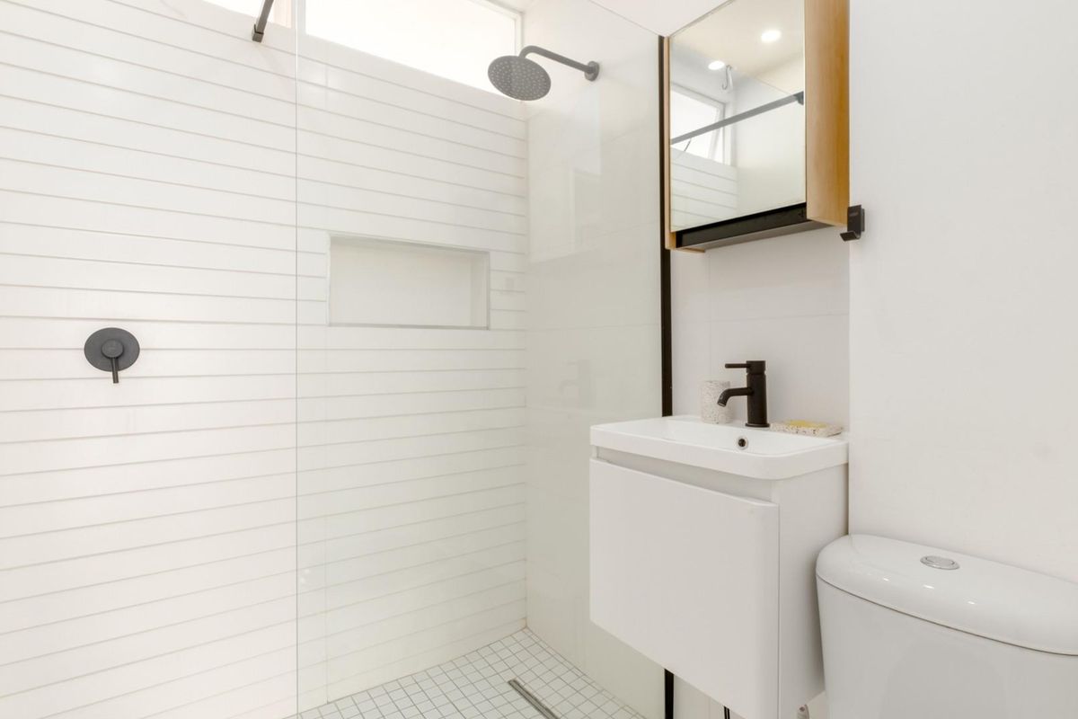Modern bathroom featuring a walk-in shower with white subway tiles, a sleek vanity with a black faucet, and a wall-mounted mirrored cabinet.