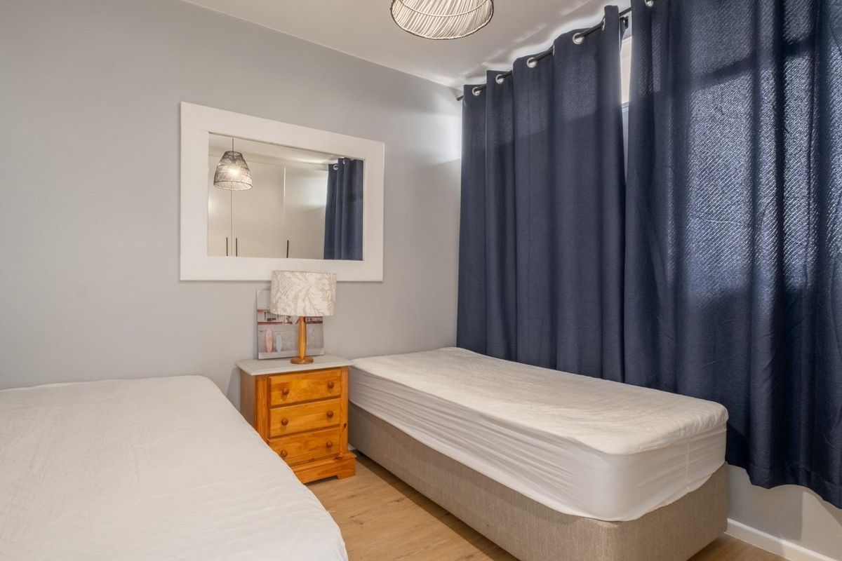 A functional bedroom featuring light wood-look flooring, neutral wall tones, and a large window dressed with dark curtains.