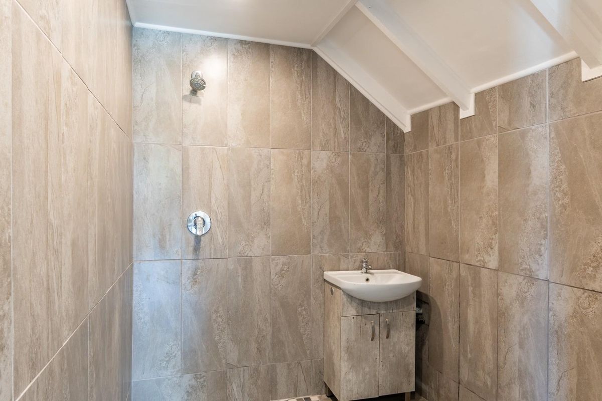 A compact bathroom featuring full-height stone-look wall tiling, a built-in shower head, and a vanity basin with storage cabinet.