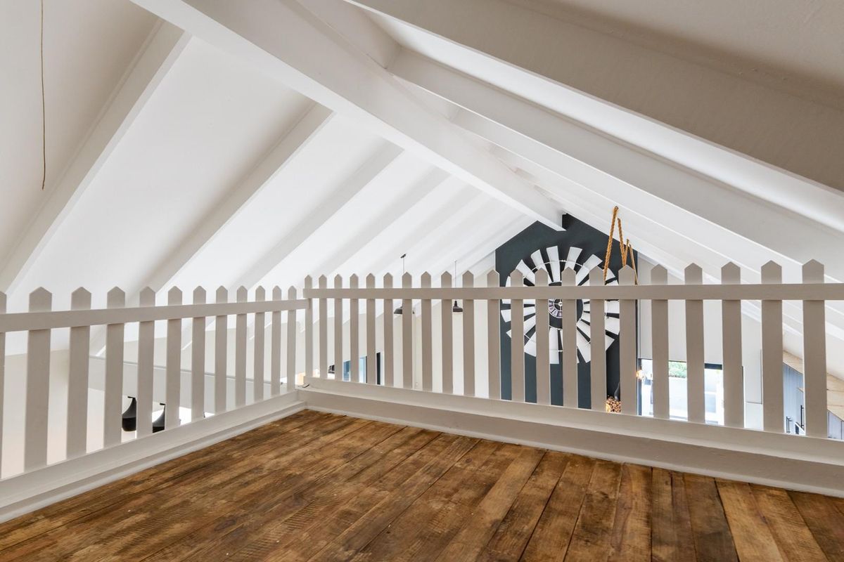 A bright mezzanine loft area featuring exposed white timber rafters, a wooden floor, and a white picket-style safety railing overlooking the lower level.
