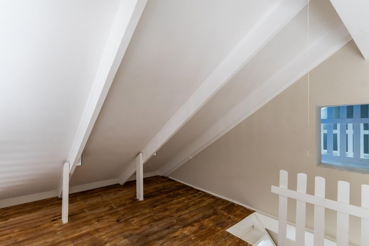 An attic-style room featuring exposed structural rafters, wooden flooring, and a small window, providing a unique architectural space.