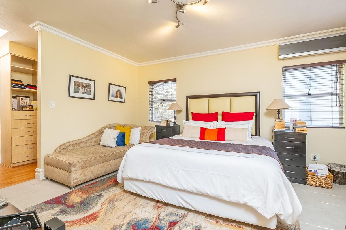Spacious bedroom featuring built-in cabinetry, wall-mounted air conditioning unit, and large windows with venetian blinds.