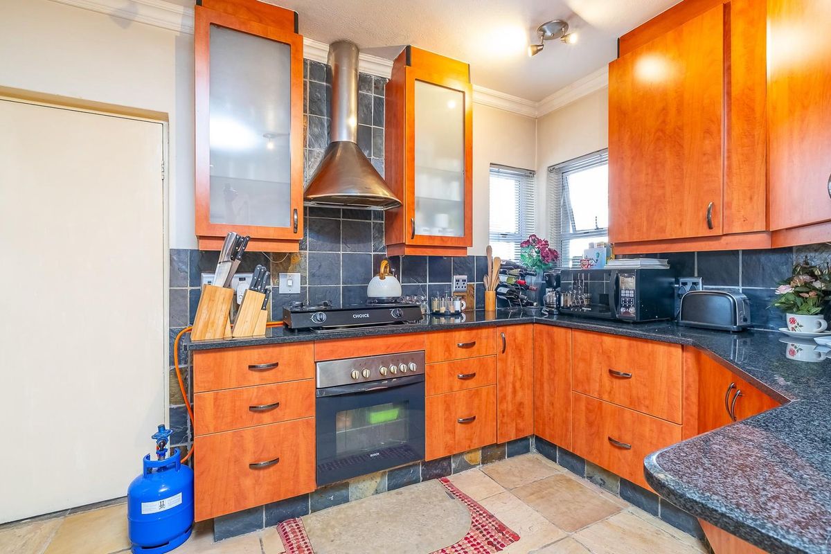 A functional kitchen featuring wooden cabinetry, dark granite countertops, a stainless steel extractor fan, and a built-in oven with gas hob.