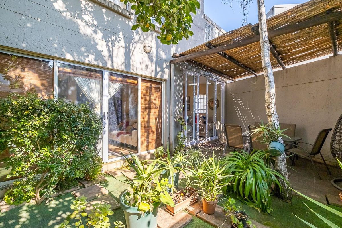 A private rear courtyard featuring a timber-slatted pergola, paved areas, and direct access to the interior living spaces through sliding glass doors.