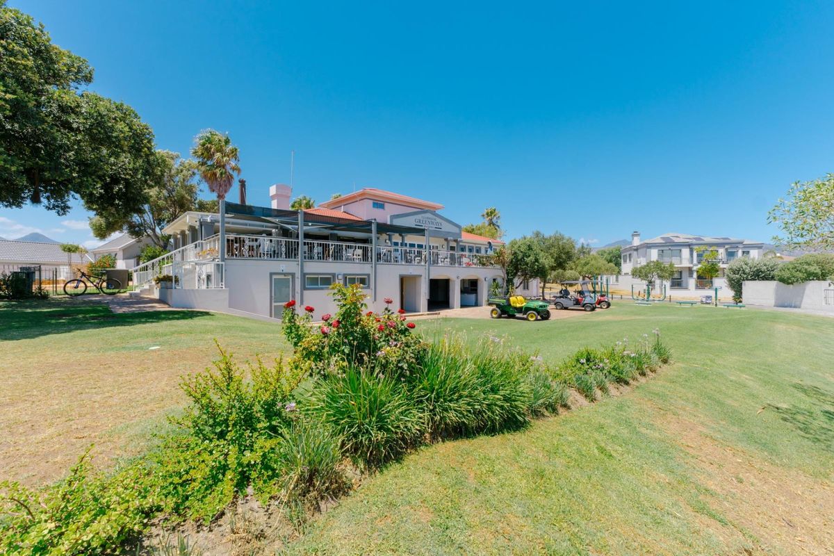 A view of the rear exterior of the clubhouse building, featuring a raised patio area, landscaped lawn, and surrounding estate grounds.