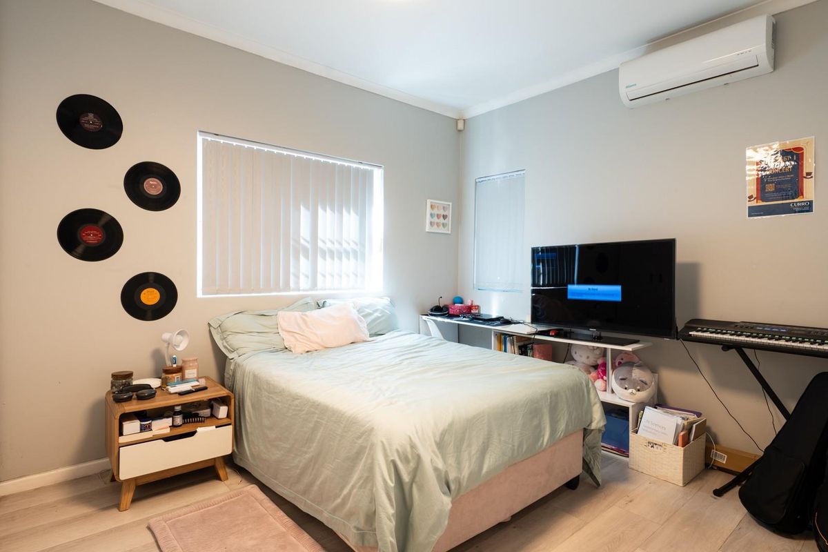 A bedroom featuring light-toned laminate flooring, vertical window blinds, and a wall-mounted air conditioning unit.