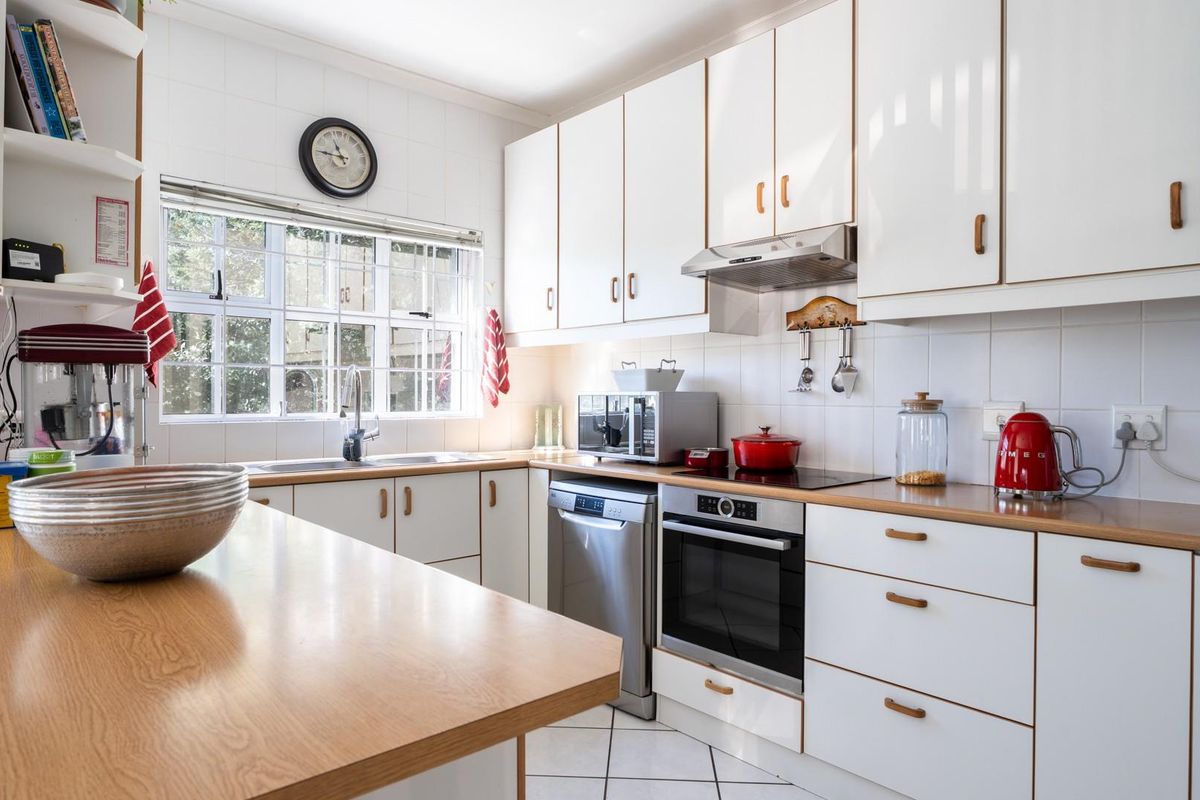 A functional kitchen featuring white cabinetry, wood-look laminate countertops, a built-in oven, electric cooktop, extractor fan, and a double sink under a window.