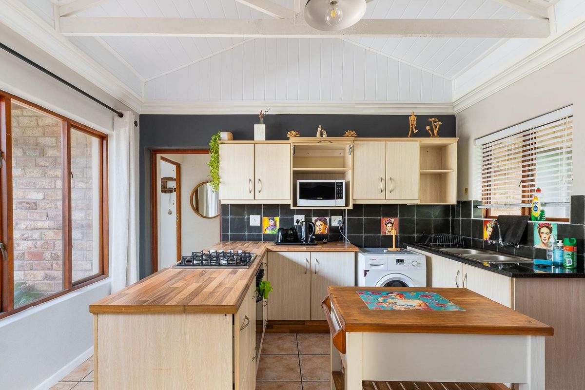 Functional kitchen featuring light wood cabinetry, dark tiled backsplash, integrated gas hob, and vaulted timber ceiling with exposed beams.