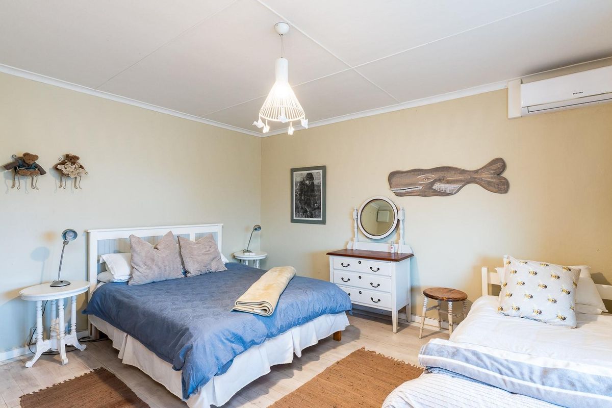 A spacious bedroom featuring light-toned flooring, a wall-mounted air conditioning unit, and a central pendant light fixture.