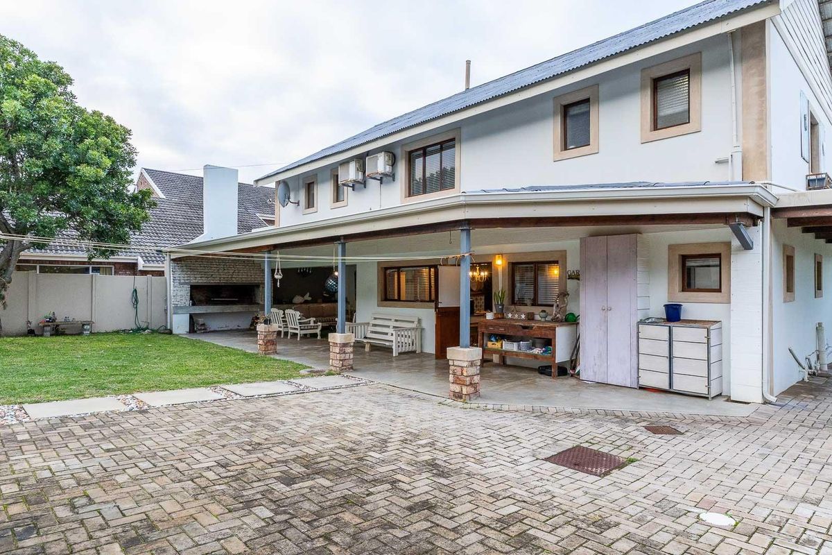 Rear exterior view featuring a covered patio area with a built-in brick braai, paved driveway, and a small lawn.