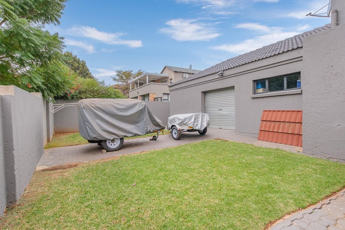 Rear exterior view of the property featuring a paved driveway, lawn area, and access to the garage.