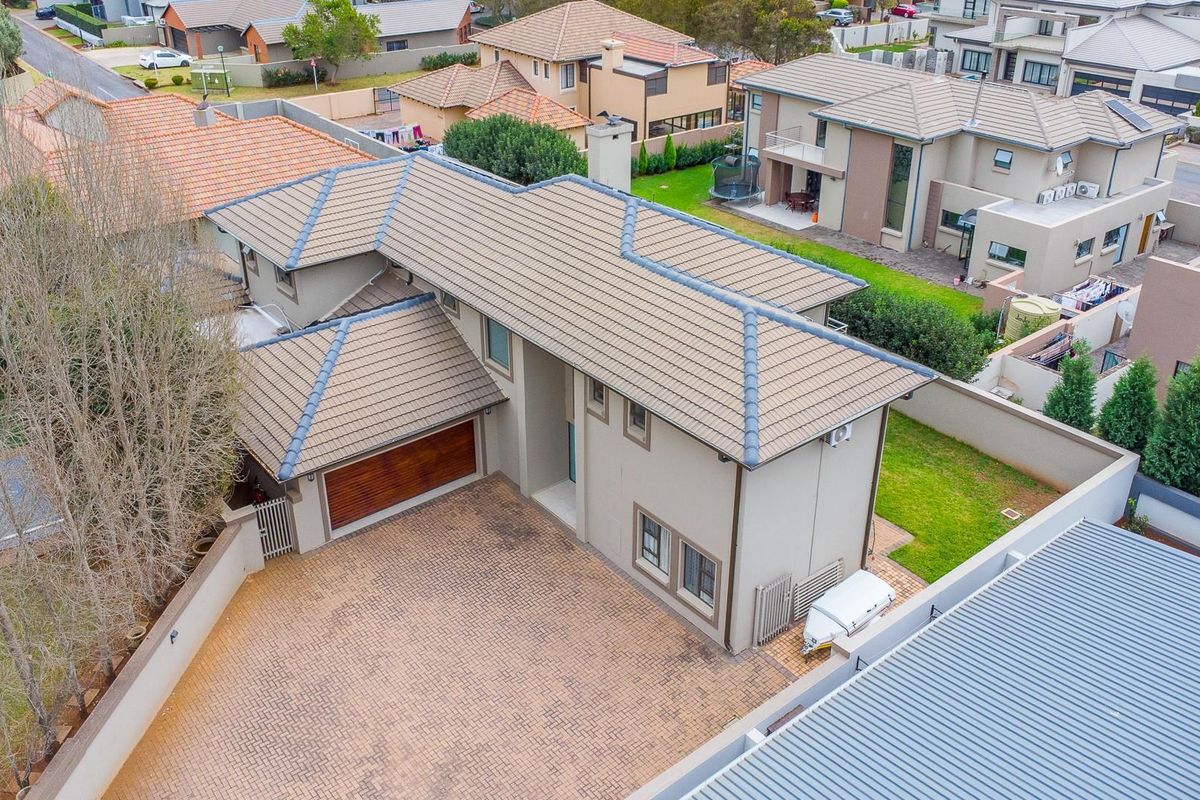 Aerial view of a modern two-story residential property featuring a paved driveway, double garage, and tiled roof within a suburban estate setting.