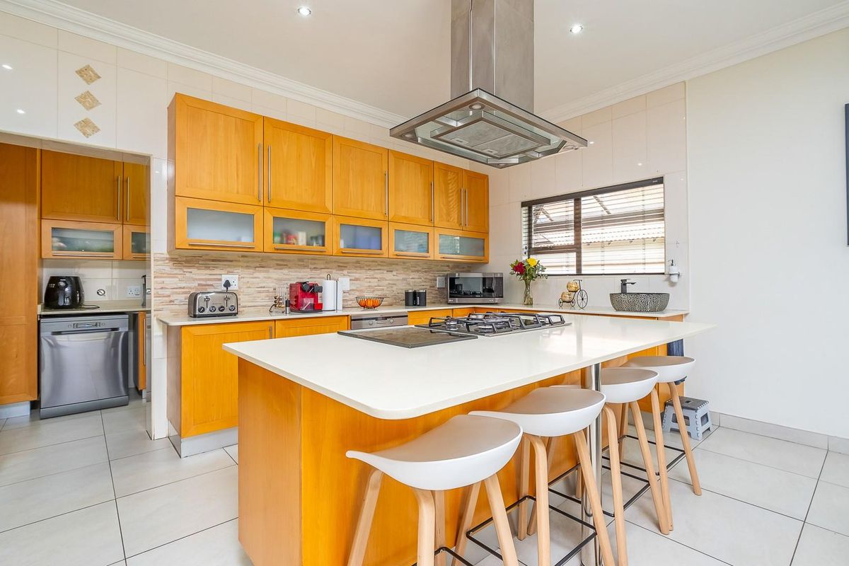 A functional kitchen featuring wooden cabinetry, a central island with a built-in gas hob, and a stainless steel extractor fan.