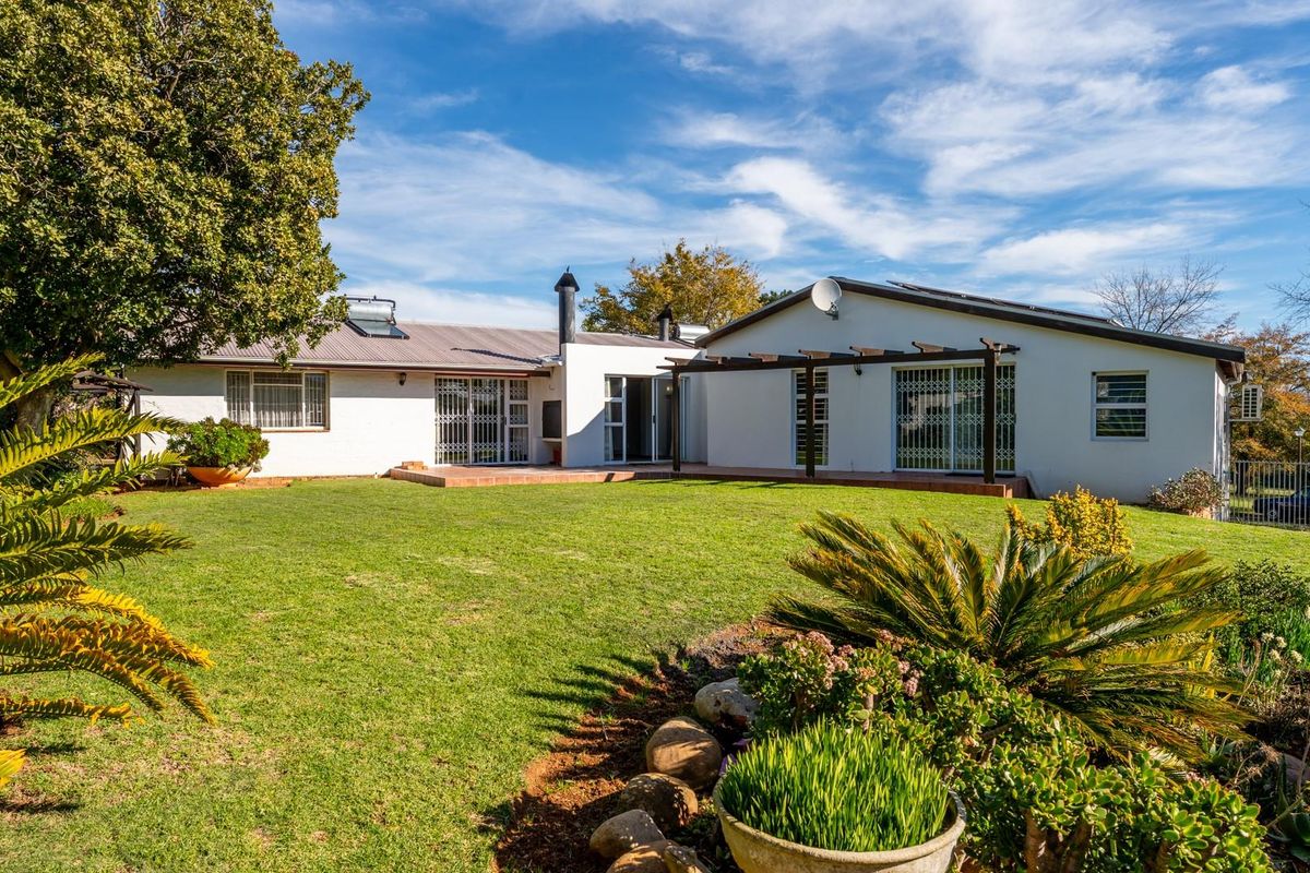 A spacious rear garden view featuring a well-maintained lawn, landscaped garden beds, and a covered patio area attached to the main house structure.