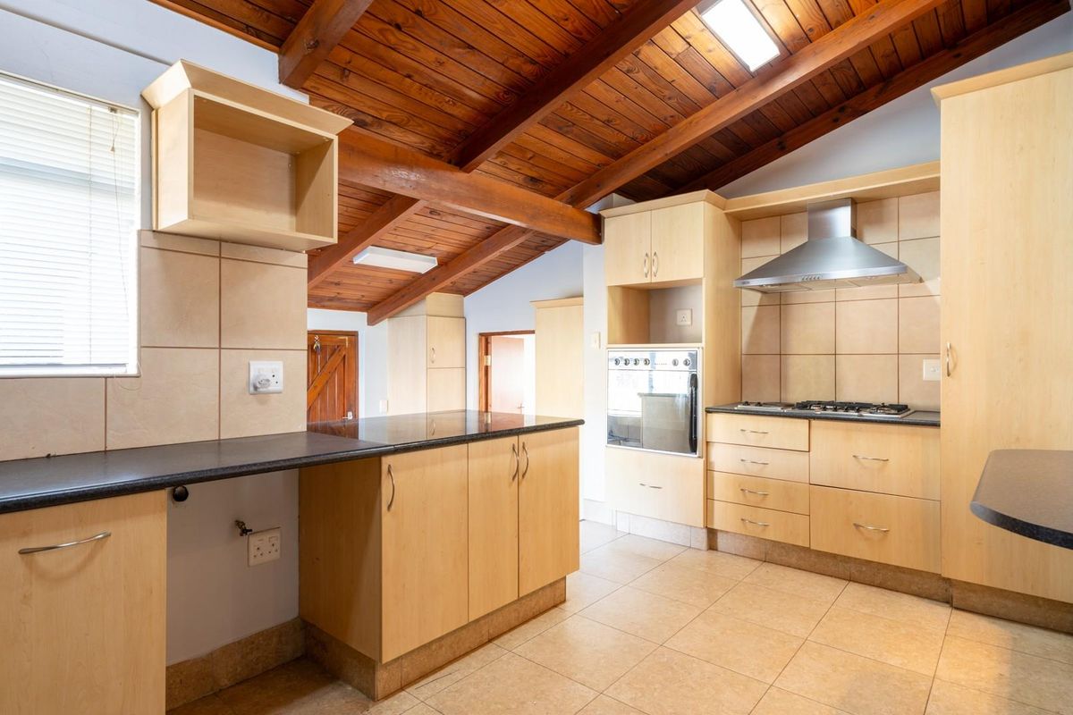 Kitchen featuring light wood cabinetry, dark countertops, built-in oven, gas hob, stainless steel extractor fan, and a vaulted timber-beamed ceiling with skylight.